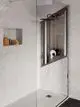 Dusche mit hängendem Regenbrausekopf, transparenten Glastüren und seitlichem Nischenregal. Installationselemente von Ideal Standard sind sichtbar hinter der Wand.
